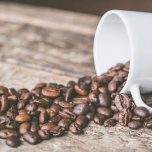 Coffee beans spilling from a white mug on a rustic wooden surface, embodying a cozy and warm atmosphere.