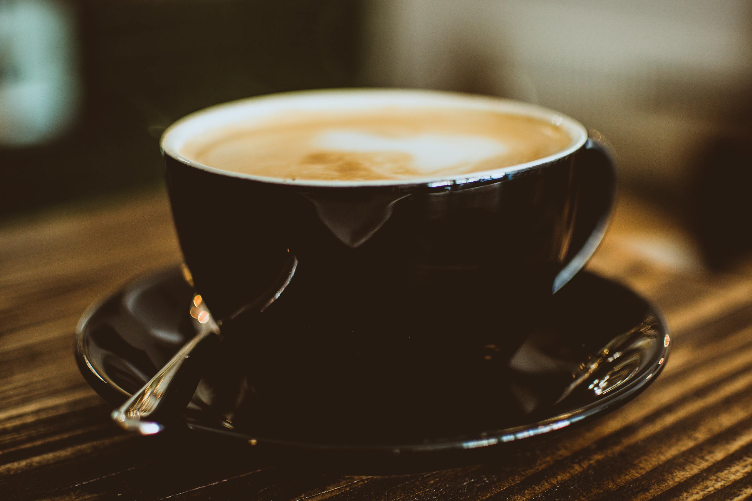 Warm espresso with cream foam served in a black ceramic cup on wooden table.