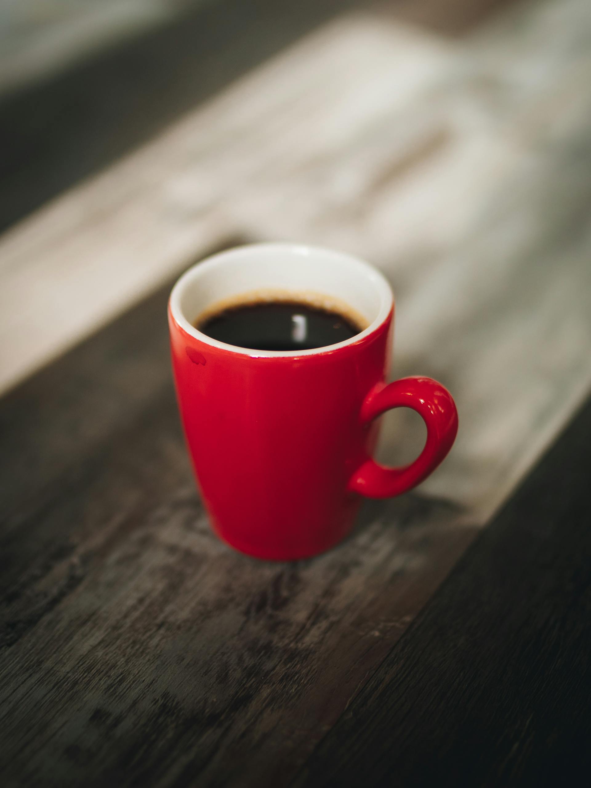 A warm cup of black coffee in a vibrant red mug on a rustic wooden table.